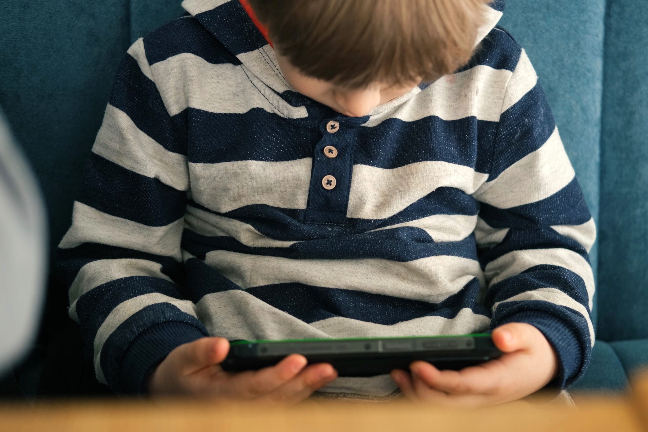 Toddler Boy looking down into his lap being distracted by the use of a cell phone, sitting at a restaurant.