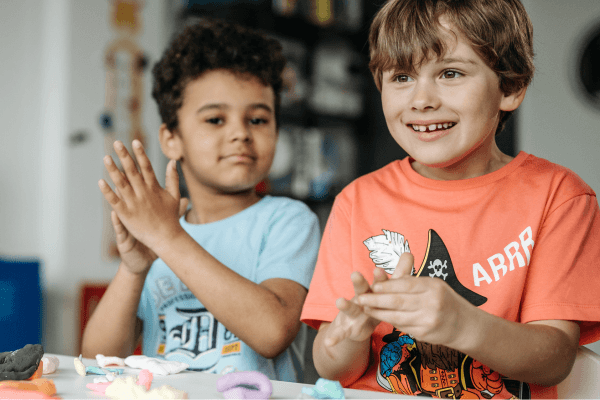 two male kids sitting at a table playing with playdoh, one smiling while exhibiting self directed play