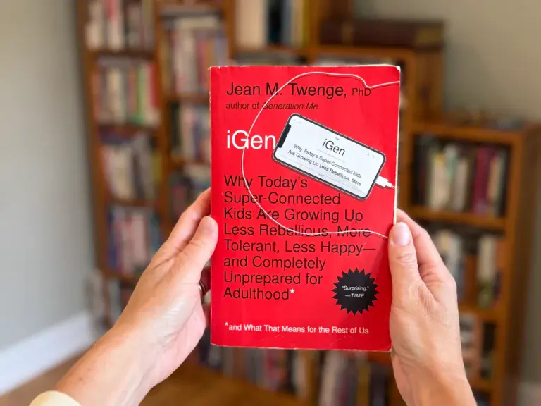 Two handing holding the red book iGen out in front of a book shelf to show what book is being reviewed.