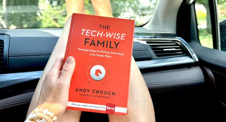 Jenna Kruse holding the book Tech Wise Family on her outstretched legs while riding in a car.