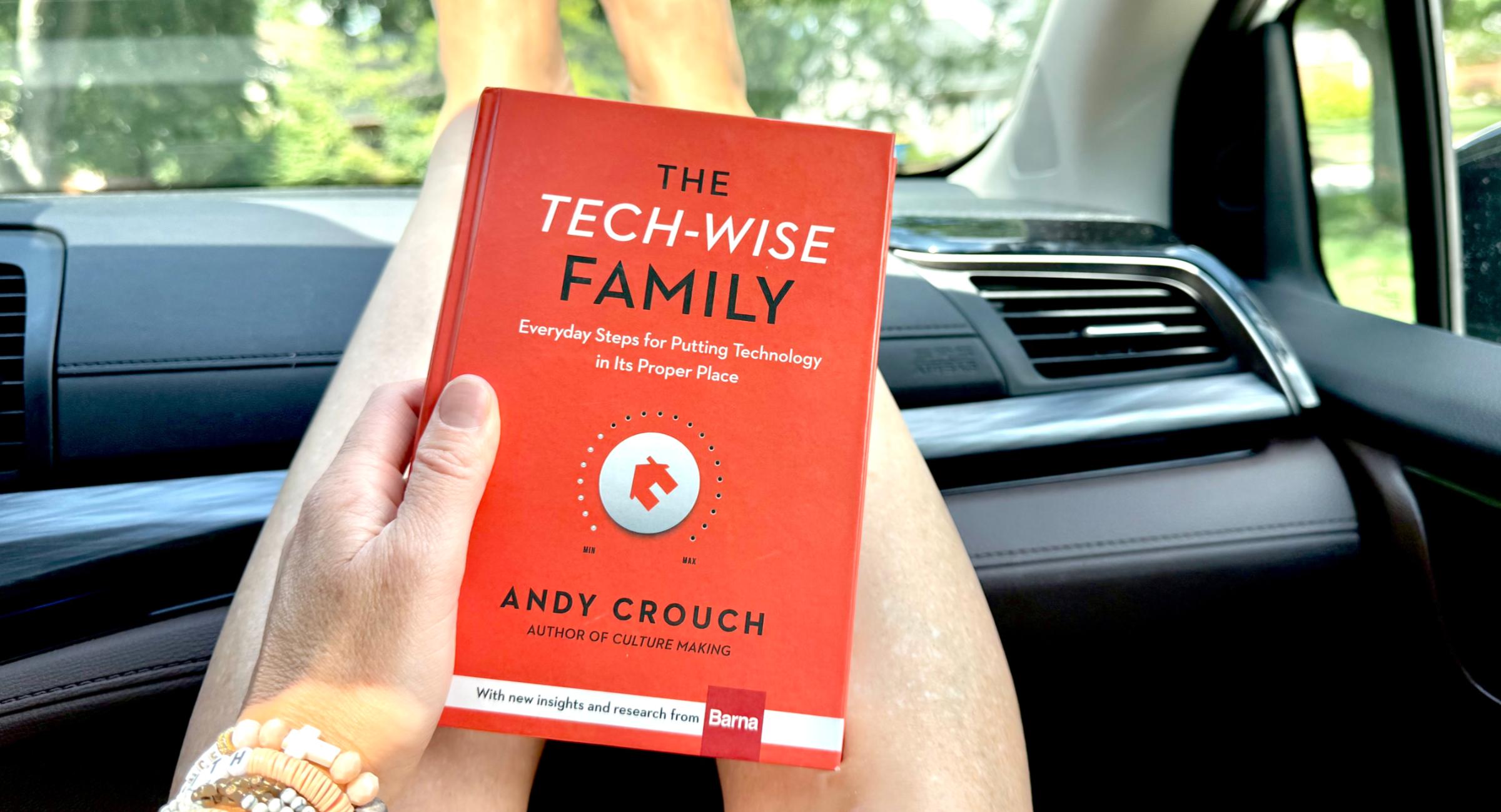Jenna Kruse holding the book Tech Wise Family on her outstretched legs while riding in a car.
