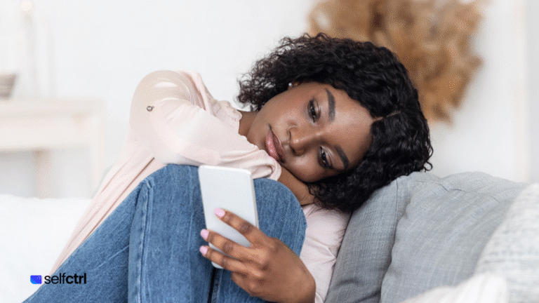 Woman sitting on the couch legs pulled in leaning her against her head against the cushion whil looking joy less scrolling social media.