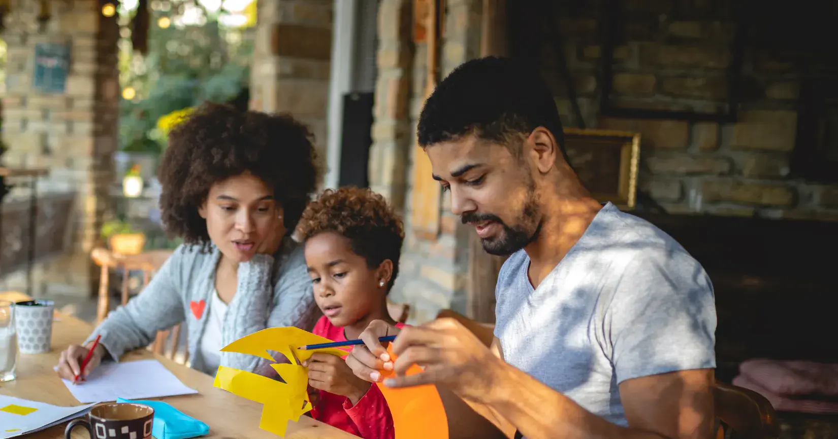 Parents do crafts with a kid at the table in their home.
